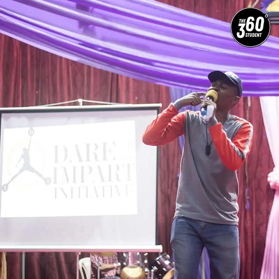A host on stage in front of the Dare to Impart Initiative screen.